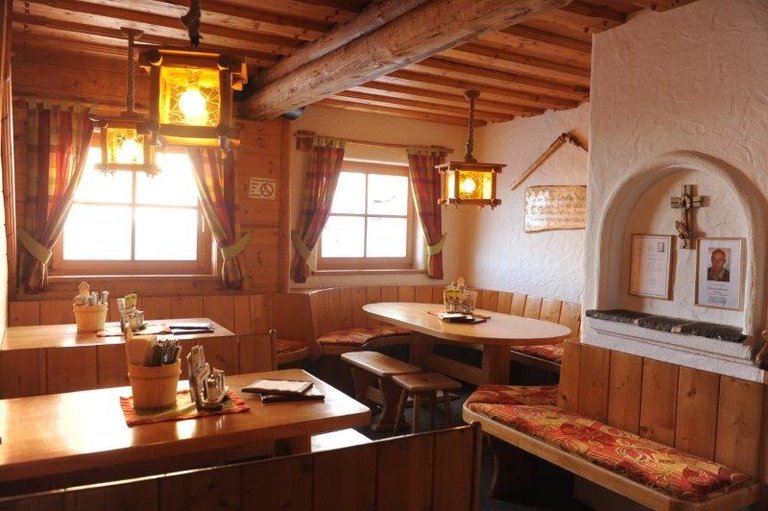 Gemütlicher Gastraum mit Holz-Polsterbänken und Holztischen, warm beleuchtet. | © Weitmoosalm