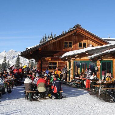 Holzhütte im Schnee mit Terrasse voll mit Menschen | © Weitmoosalm