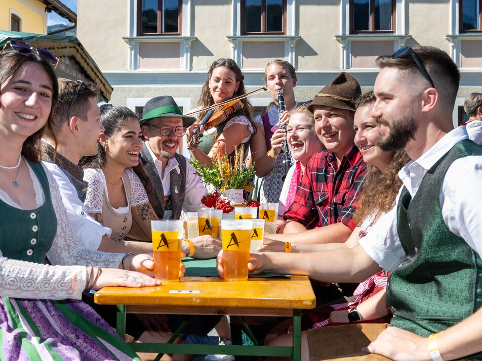 In Tracht gekleidete Männer und Frauen mit Getränken und Musikinstrumenten. | © ARGE Aicher Kirtag©Harald Steiner