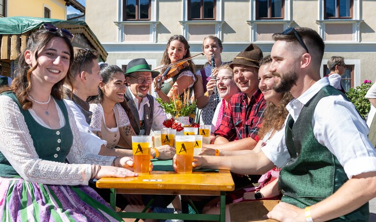 In Tracht gekleidete Männer und Frauen mit Getränken und Musikinstrumenten. | © ARGE Aicher Kirtag©Harald Steiner