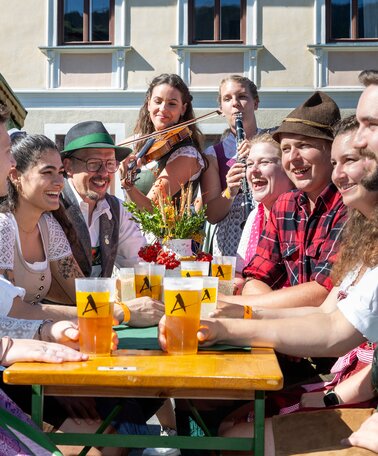 In Tracht gekleidete Männer und Frauen mit Getränken und Musikinstrumenten. | © ARGE Aicher Kirtag©Harald Steiner