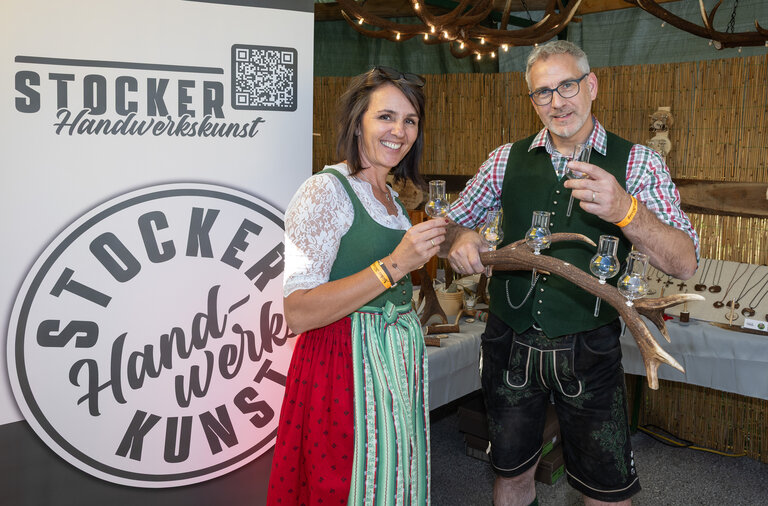 2 in Tracht gekleidete Personen, die selbstgemachte Handwerkskunst aus Hirschhorn präsentieren. | © ARGE Aicher Kirtag©Harald Steiner