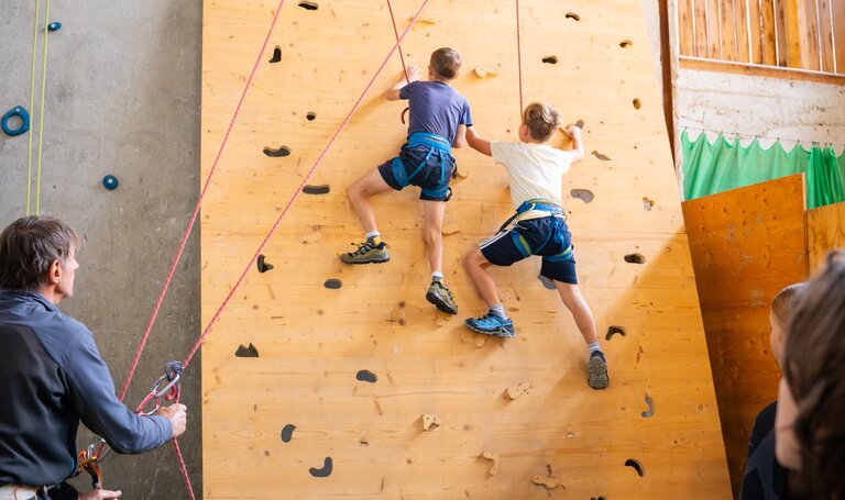 Zwei Kinder klettern gesichert an einer Indoor-Kletterwand, Erwachsene sichern und schauen zu. | © TVB/Laura Passenbrunner