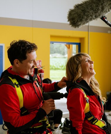 Eine Frau und ein Mann in Bergrettungsoutfit, die herzlich lachen. | © ZDF_2024_17. Staffel