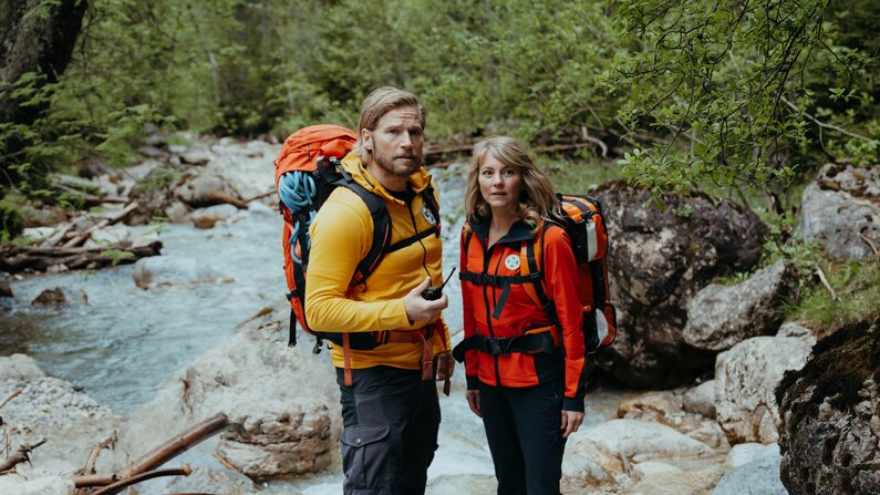 Eine Frau und ein Mann in Bergrettungskleidung stehen in einem Flussbett  | © ZDF_2024_17. Staffel
