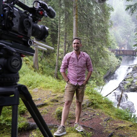 Moderator Richard Deutinger vor der Kamera, Anmoderation am Riesachfall, aufgenommen | © ServusTV / Brigitte Erhart / Degn Film