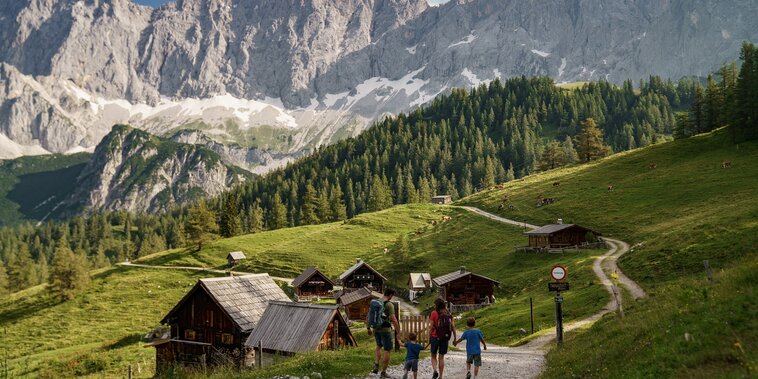 Neustattalm mit dem Dachsteinmassiv im Hintergrund und einer Familie, die in Richtung Neustattalm wandert | © Christine Höflehner